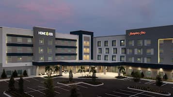 A hotel with a modern design, featuring a 'Home Suites by Hilton' and 'Hampton Inn' sign, a spacious parking lot, and a well-lit entrance area.