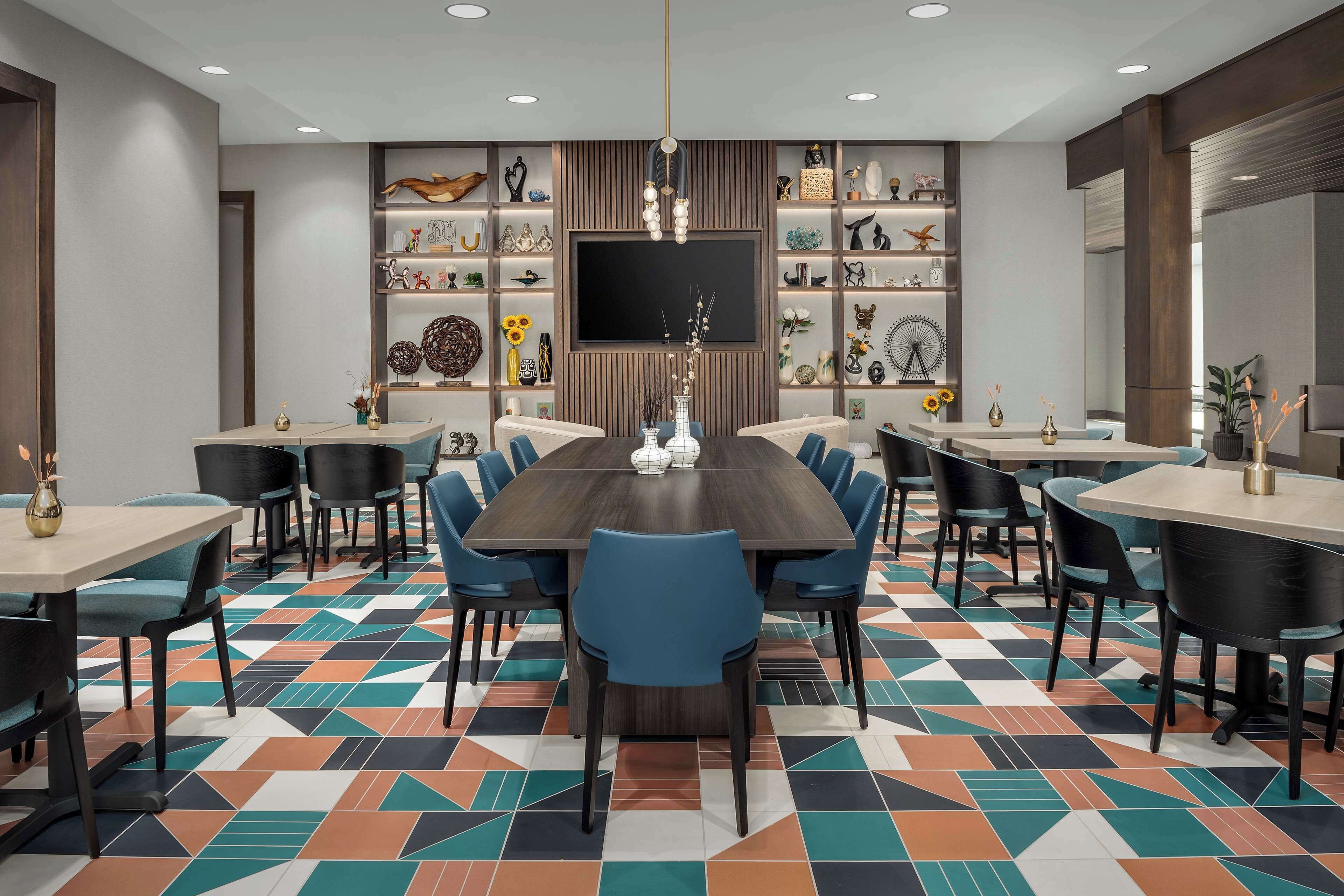 Een vergaderzaal met een grote houten tafel, blauwe stoelen en een vloer met een patroon.