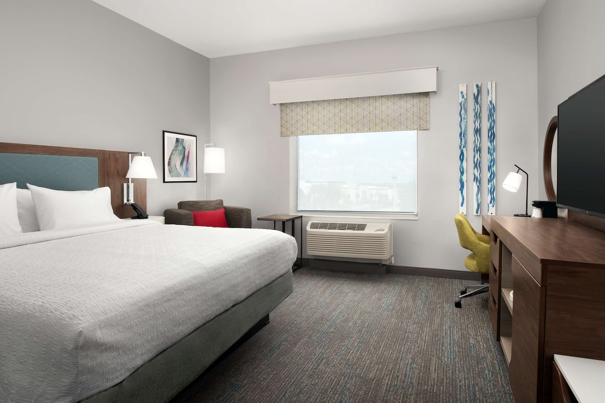 A hotel room with a large bed, a desk, a chair, a TV, and a window with curtains.