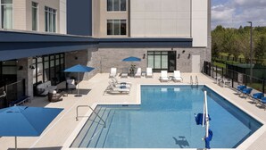 Un área de piscina en la azotea con sillones y sombrillas, rodeada por un edificio de amplios ventanales y fachada de piedra.