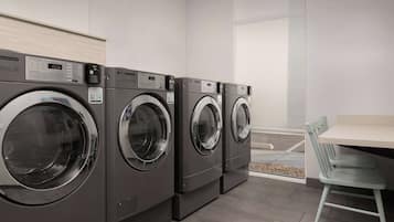 A row of commercial washers in a clean, modern laundry room with a small table and chair.