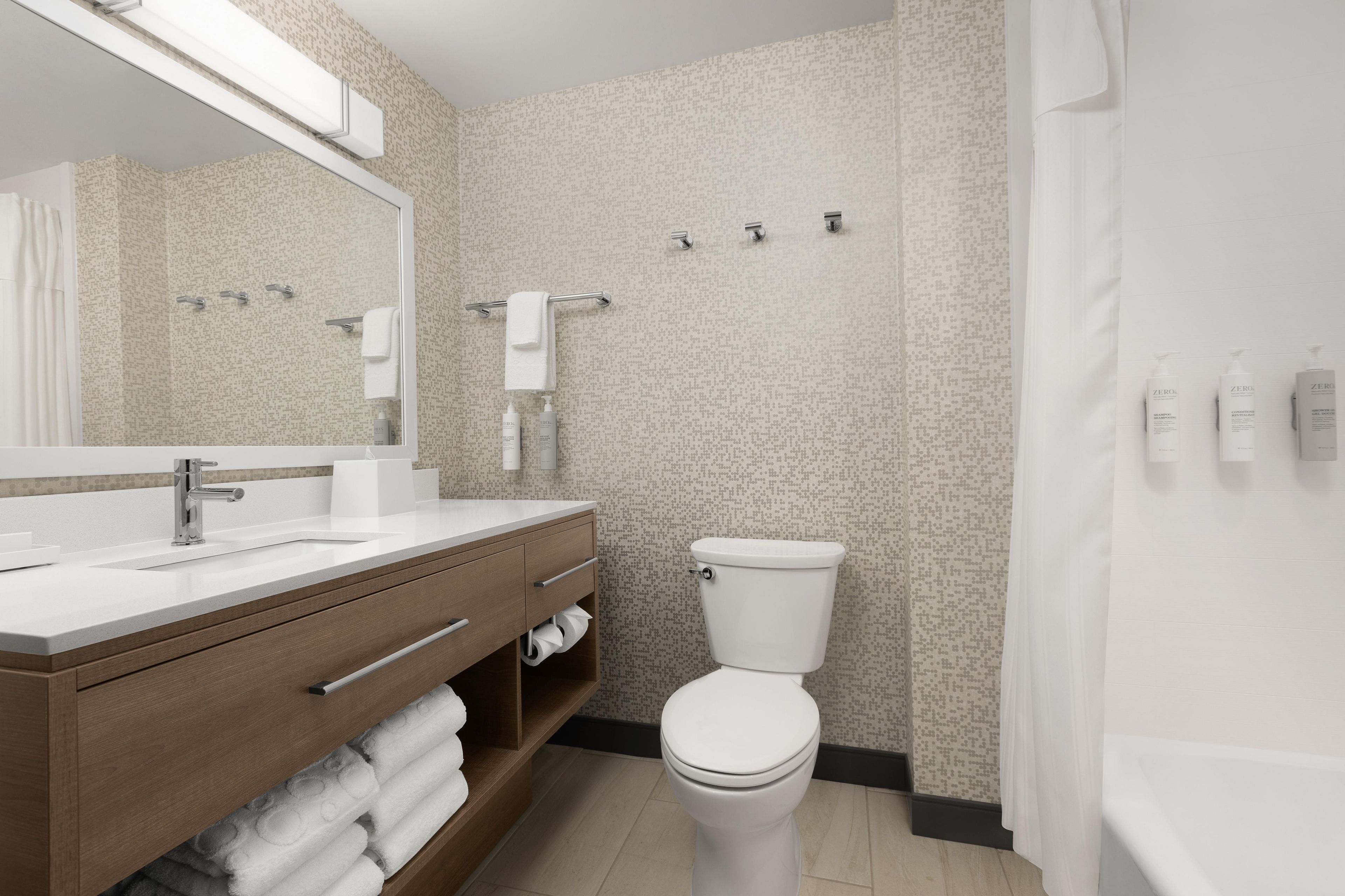 A modern bathroom with a large mirror, a sink with a wooden vanity, a toilet, and a shower area.