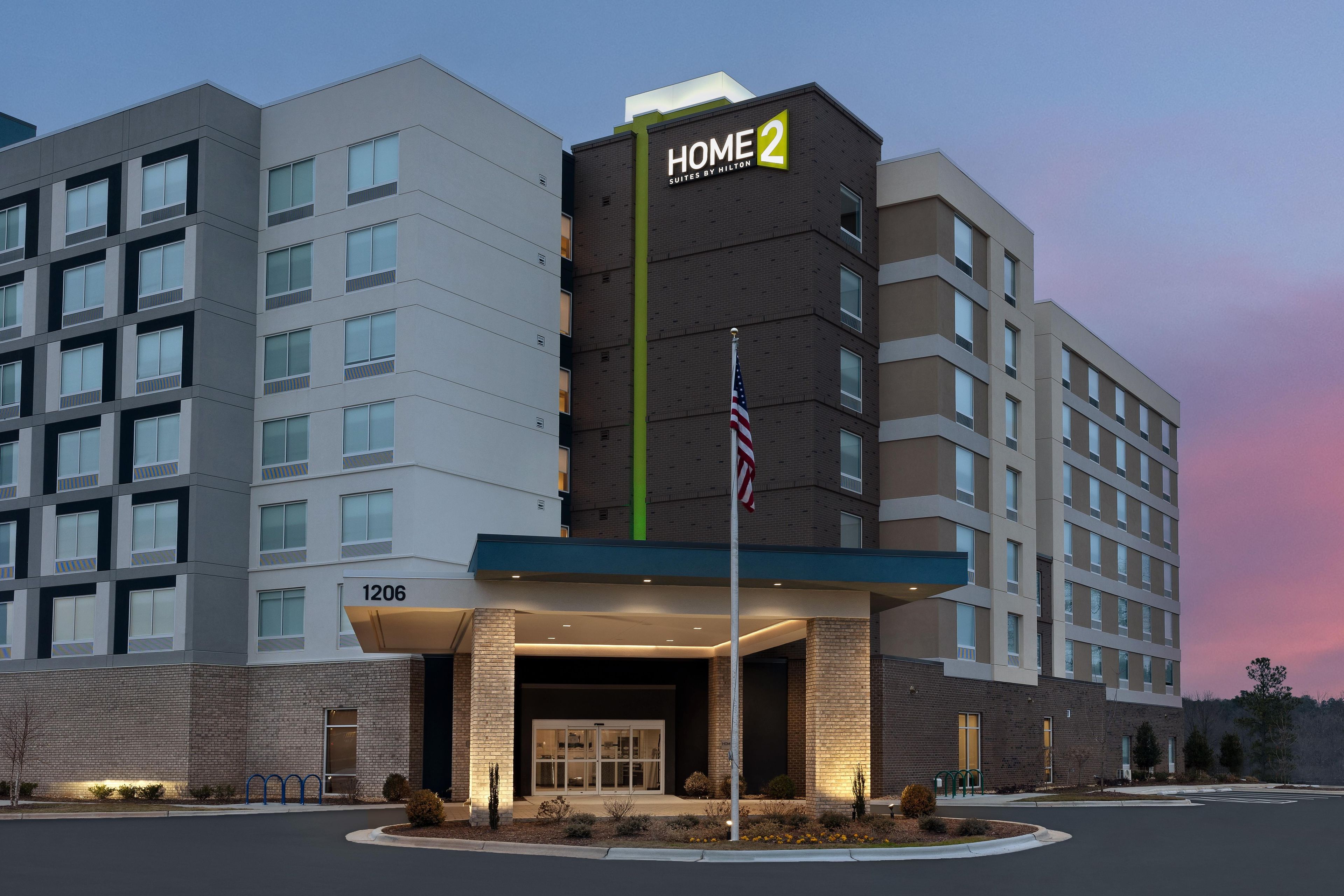 A multi-story hotel with a prominent 'HOME 2' sign, a brick facade, and a well-lit entrance.