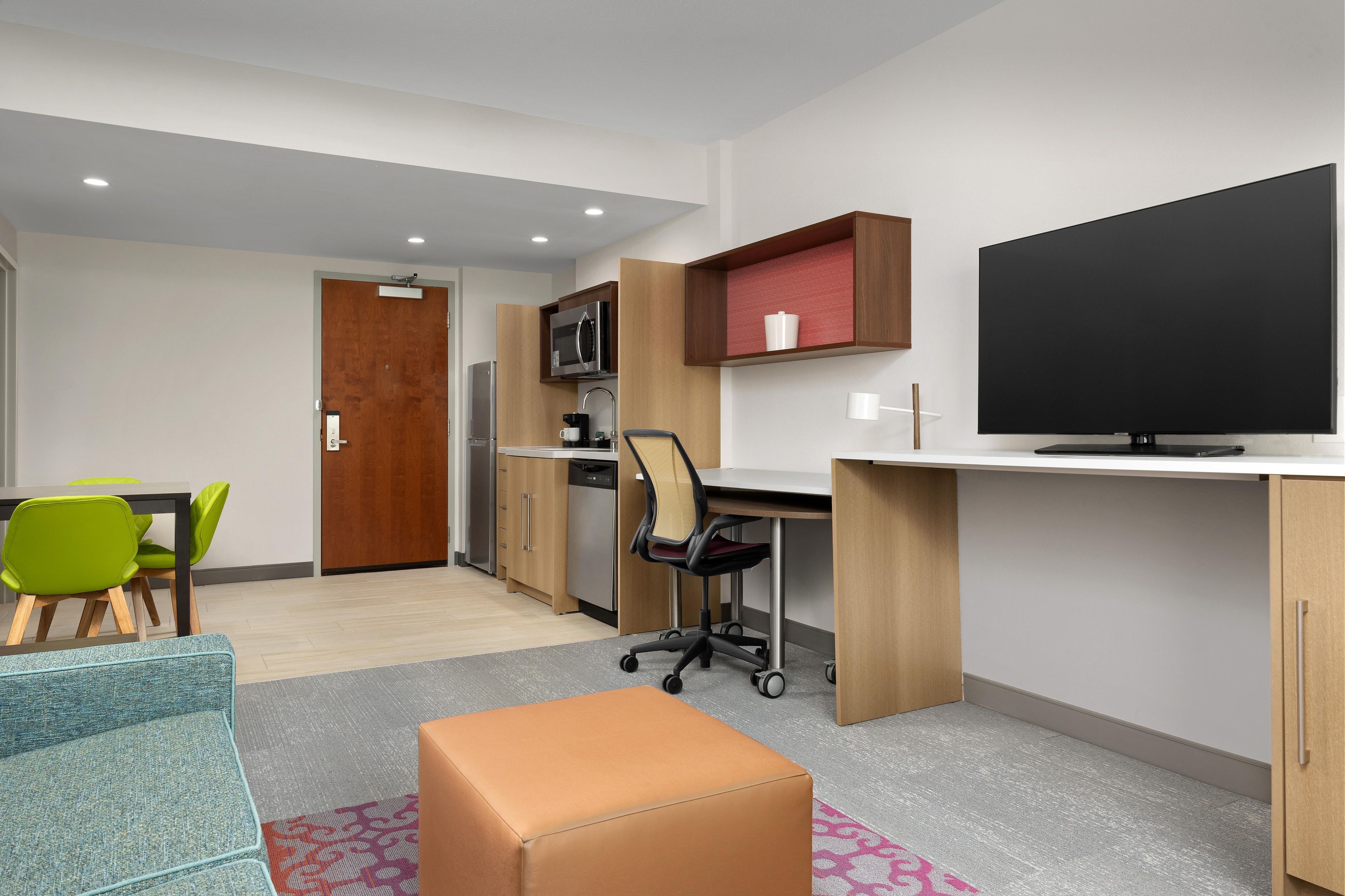 Une chambre moderne équipée d’un bureau, d’une chaise, d’une télévision, d’une kitchenette et d’une porte.