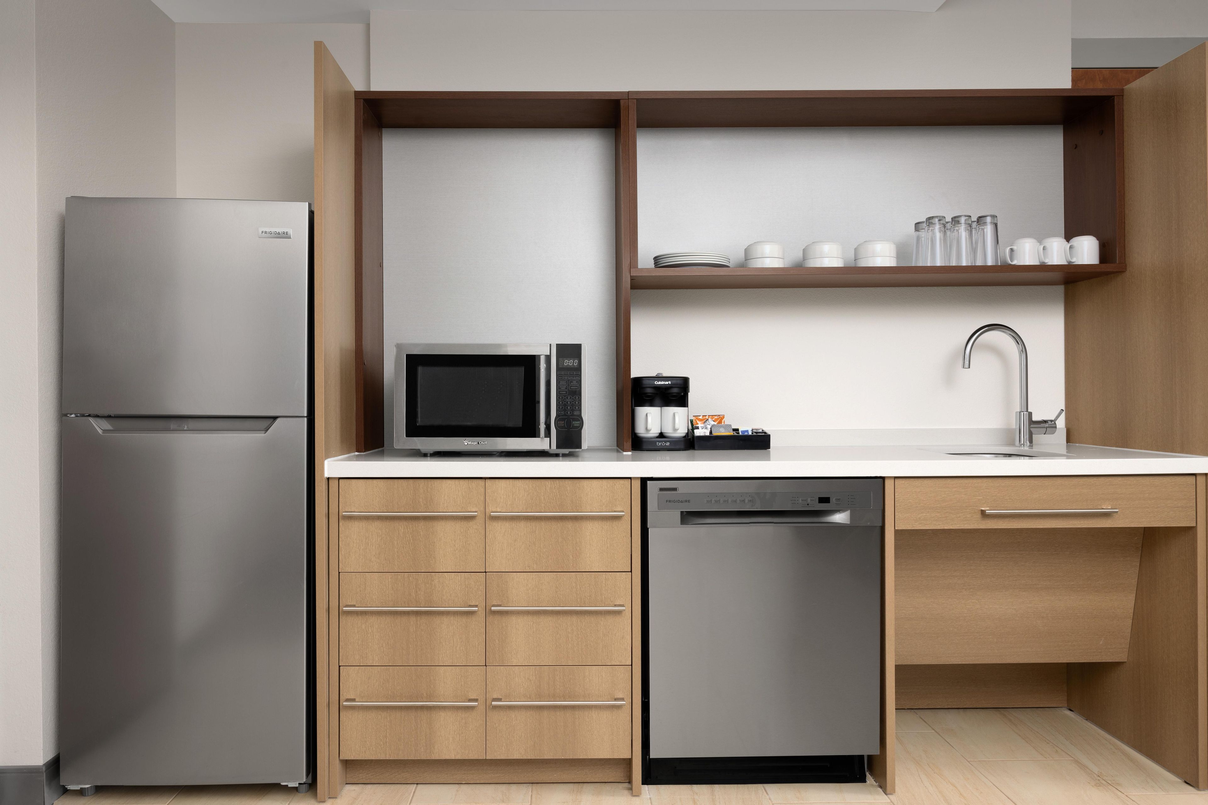 Cozinha compacta com geladeira de aço inoxidável, micro-ondas, máquina de café e lava-louças.