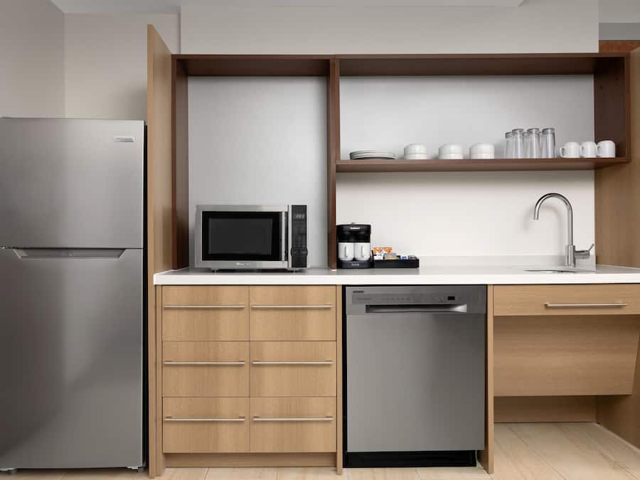 A compact kitchen with a stainless steel refrigerator, a microwave, a coffee maker, and a dishwasher.