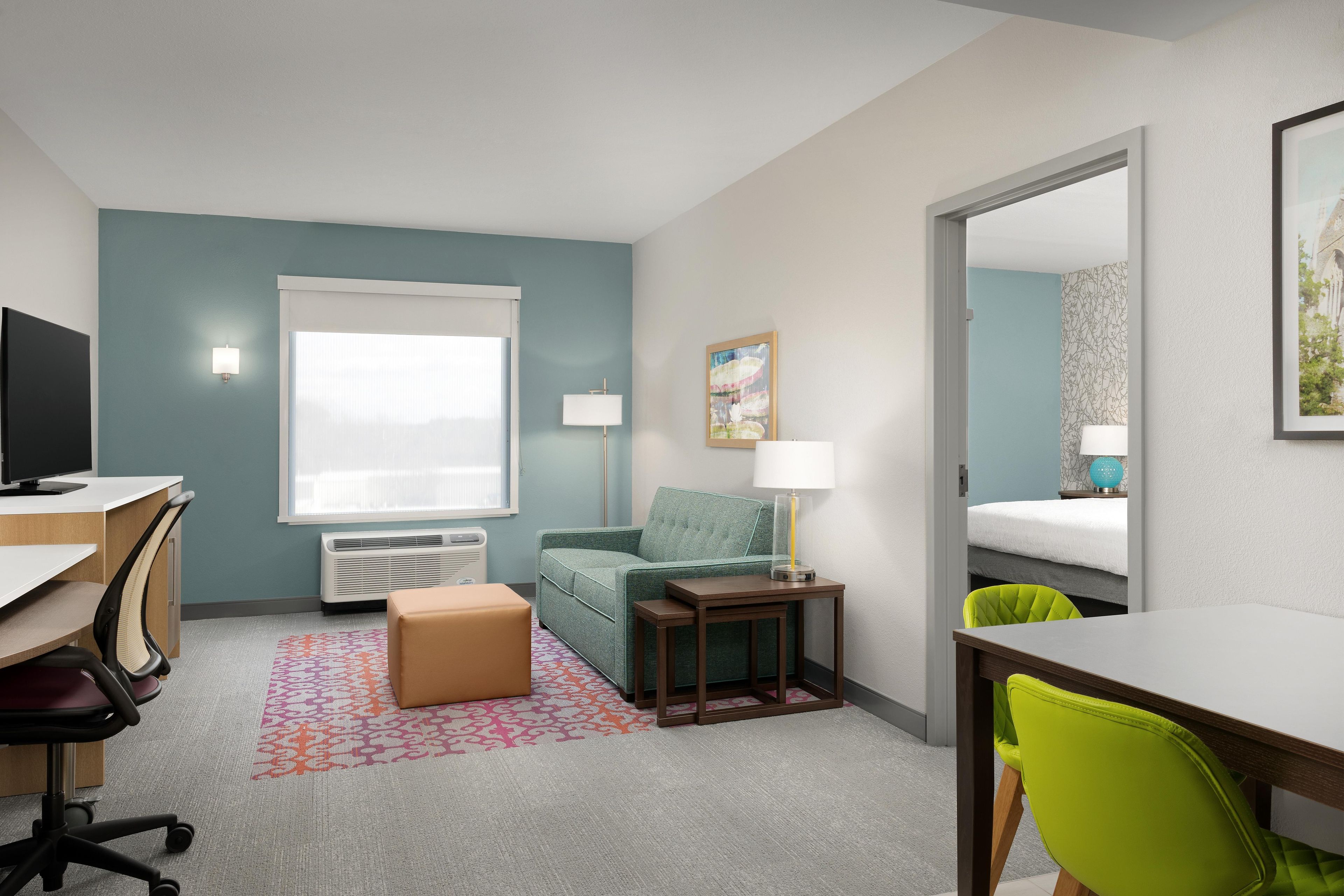 A hotel room with a desk, chair, sofa, bedside table, lamp, and a bed.