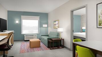 A hotel room with a desk, chair, sofa, bedside table, lamp, and a bed.