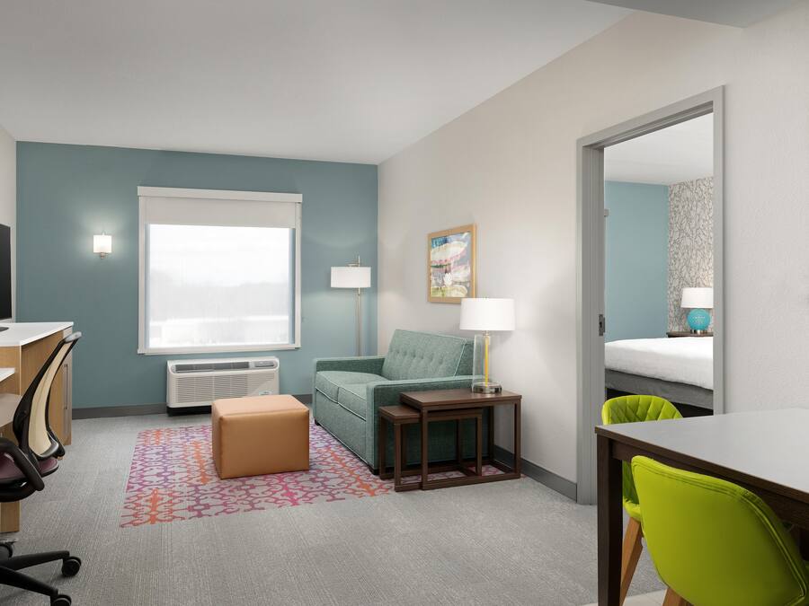 A hotel room with a desk, chair, sofa, bedside table, lamp, and a bed.