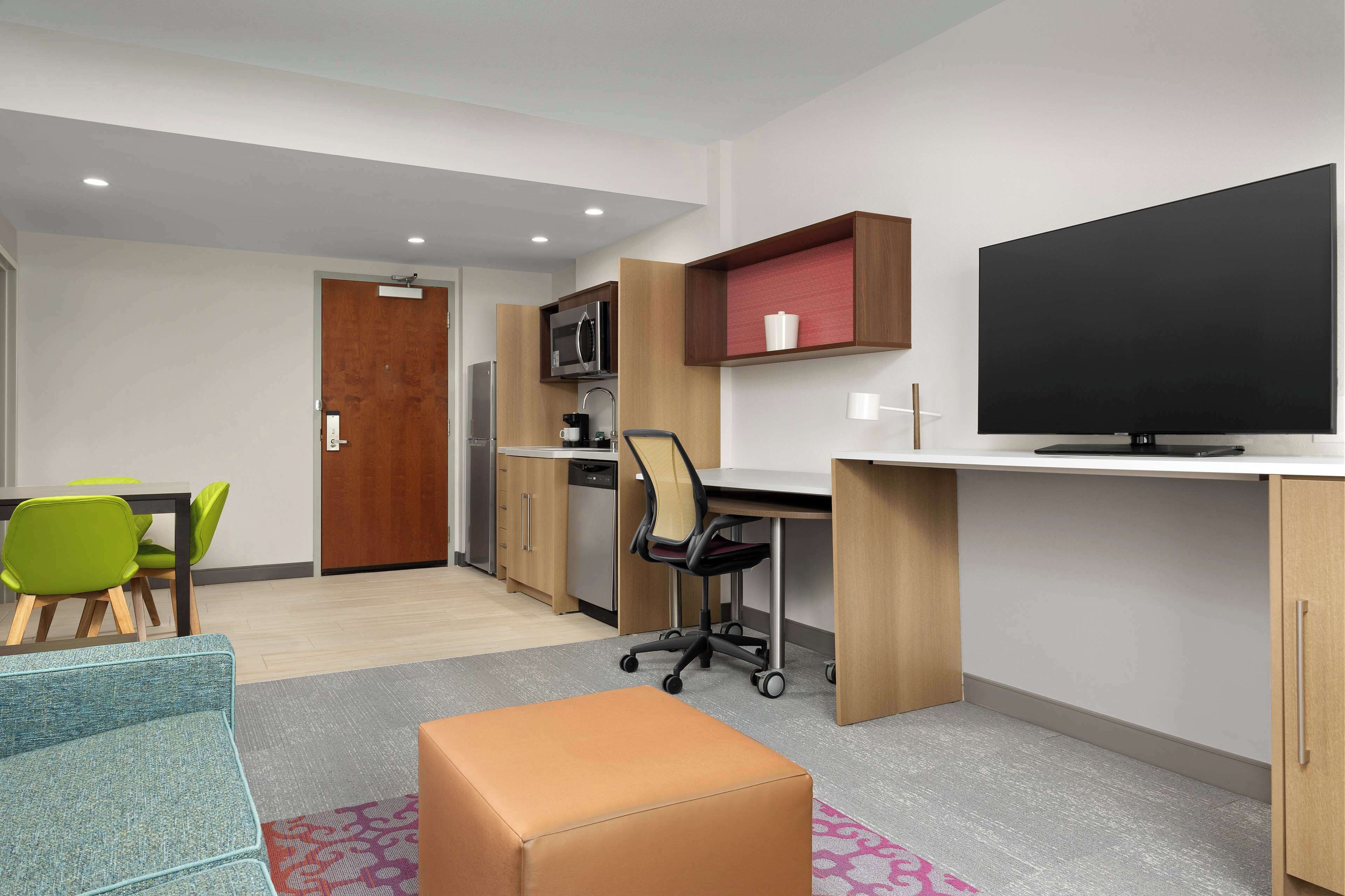 A modern room with a desk, chair, television, and kitchenette.
