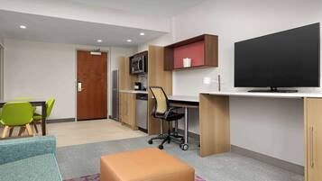 A modern room with a desk, chair, television, and kitchenette.