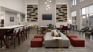 A modern dining area with a long table, multiple chairs, and a sofa with red ottomans. - Hampton Inn & Suites Durham University Medical Center (Durham)