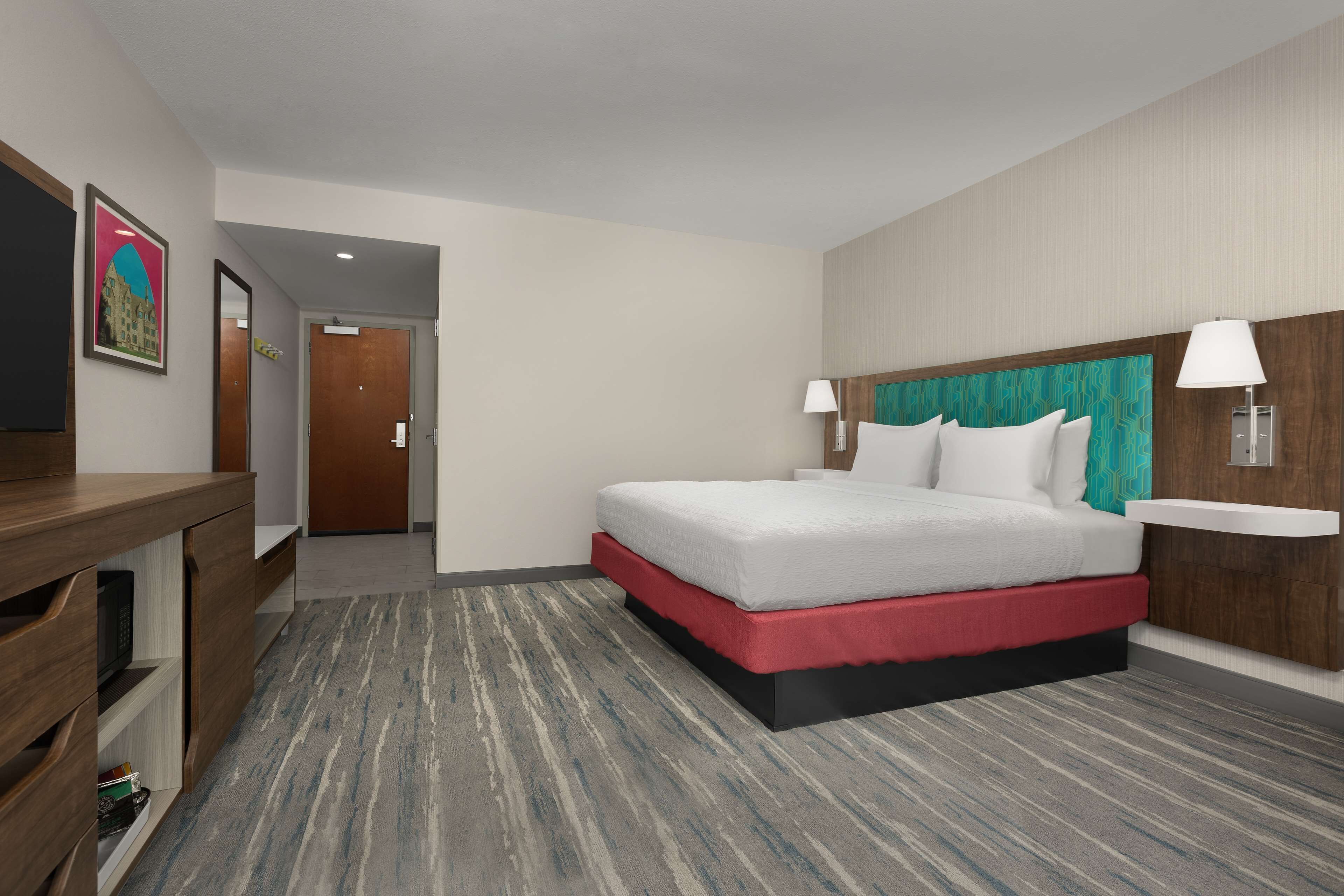 A hotel room with a bed, bedside lamps, a desk with a chair, and a television.