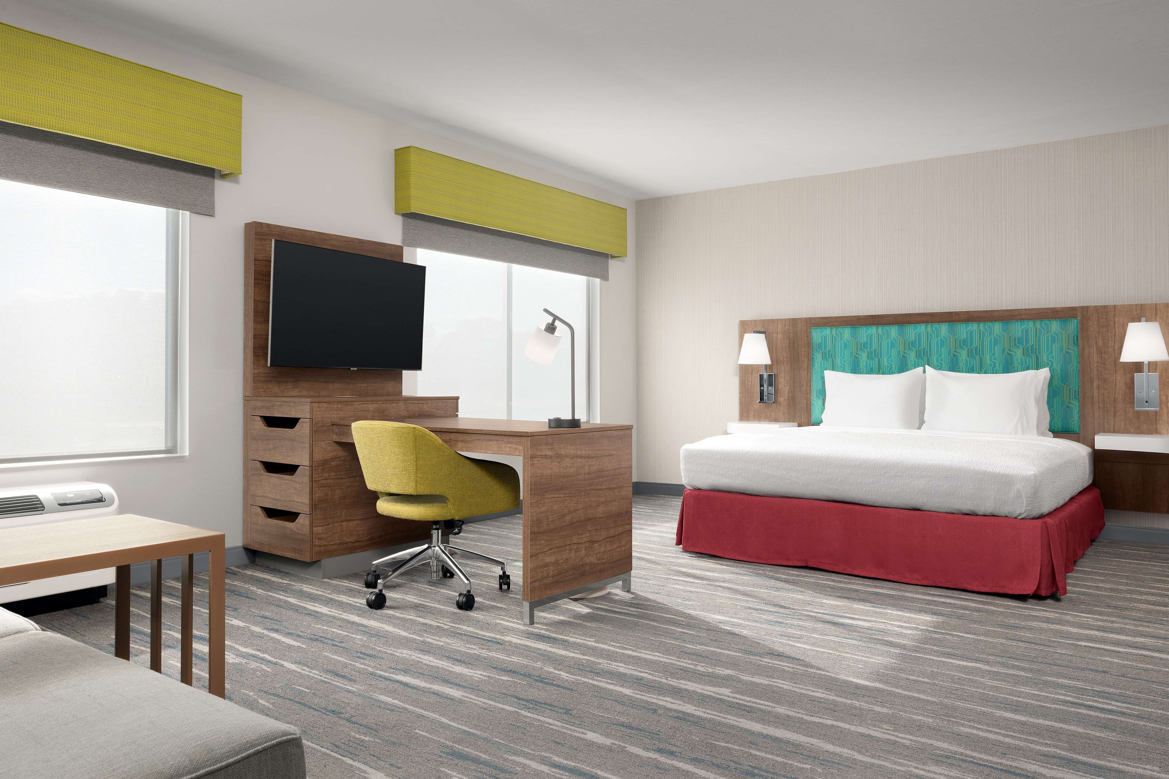 A hotel room with a bed, desk, chair, television, and a window.