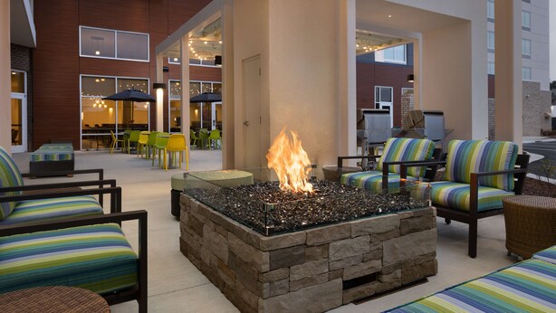 A stone fire pit surrounded by striped chairs and tables in an outdoor lounge area with a view of a building in the background. - Hampton Inn & Suites Durham University Medical Center (Durham)