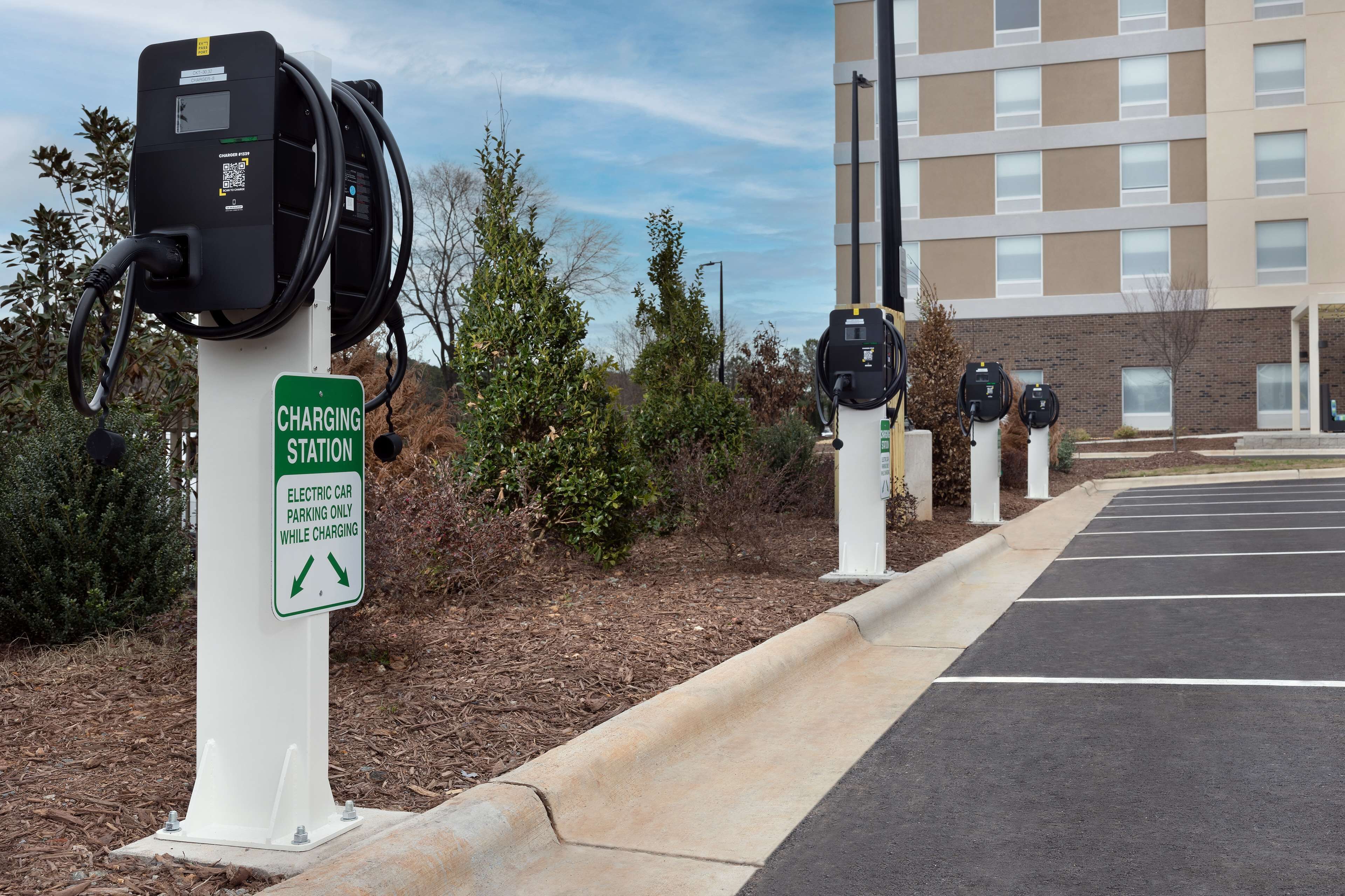 Un área de estacionamiento con estaciones de carga para coches eléctricos y un cartel que indica que el estacionamiento solo está permitido durante la carga.