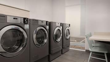 A row of commercial washers in a clean, modern laundry room with a small table and chair.