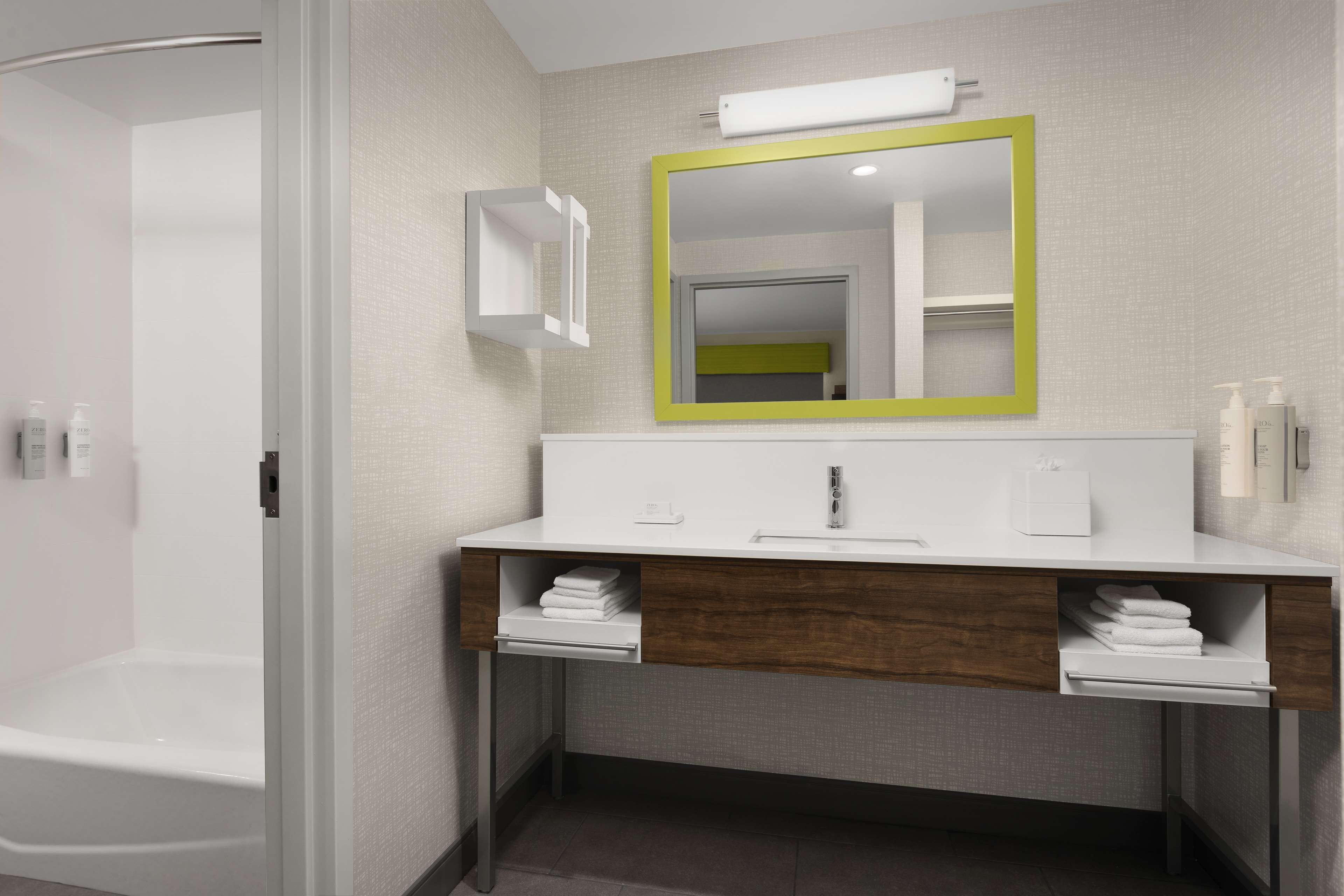 A modern bathroom with a white vanity, a mirror with a green frame, and a shower area.
