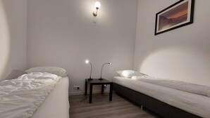 Een ruime, goed verlichte kamer met twee eenpersoonsbedden, een bureau met lamp en een schilderij aan de muur.