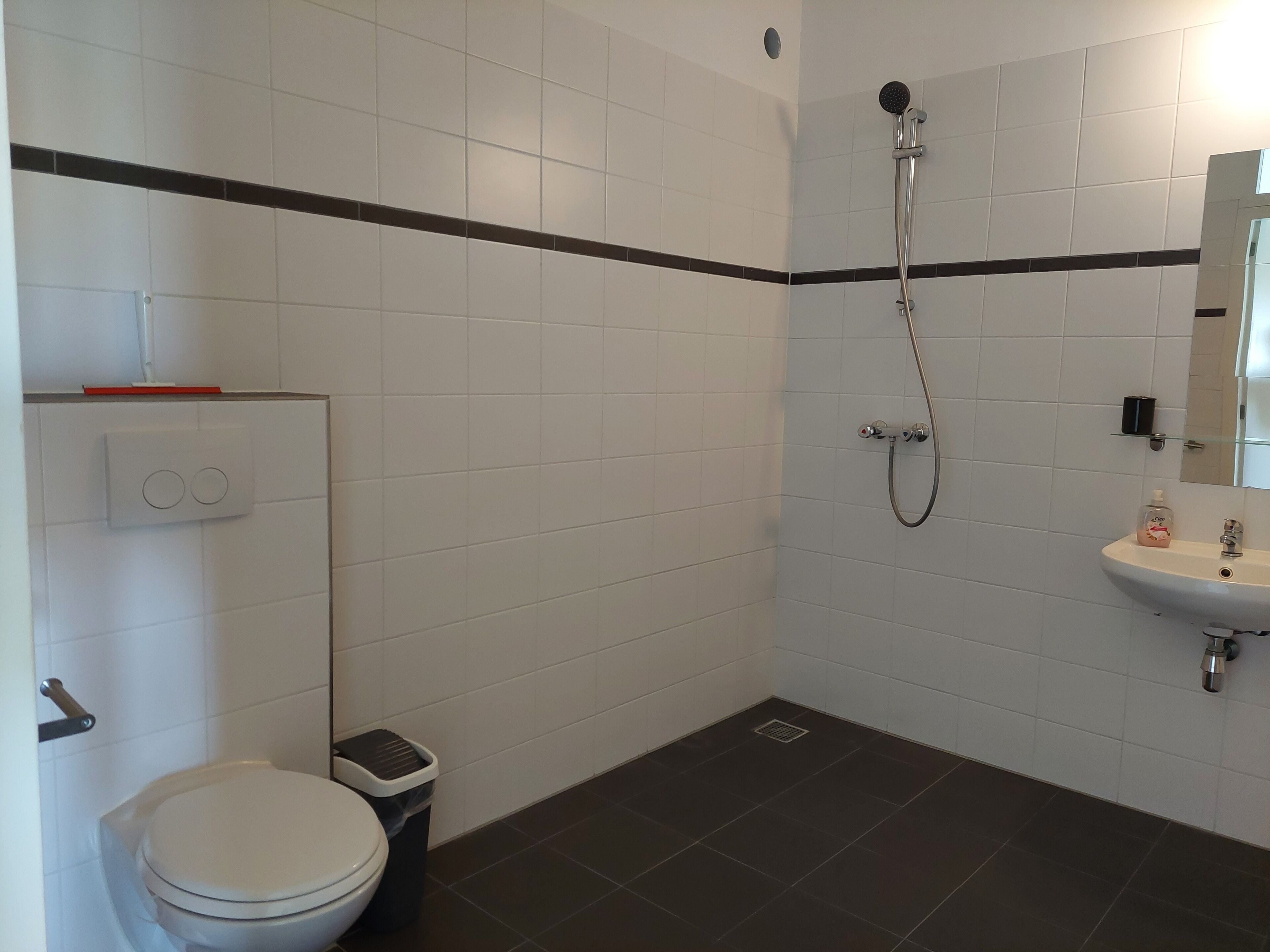 A bathroom with a toilet, a trash bin, a shower, and a sink.