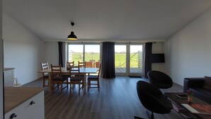 Een moderne woonkamer met een eethoek, een flatscreen televisie en uitzicht op een groen veld.