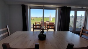 Een eethoek met een houten tafel en stoelen, een potplant en uitzicht op een grasveld door grote glazen deuren.