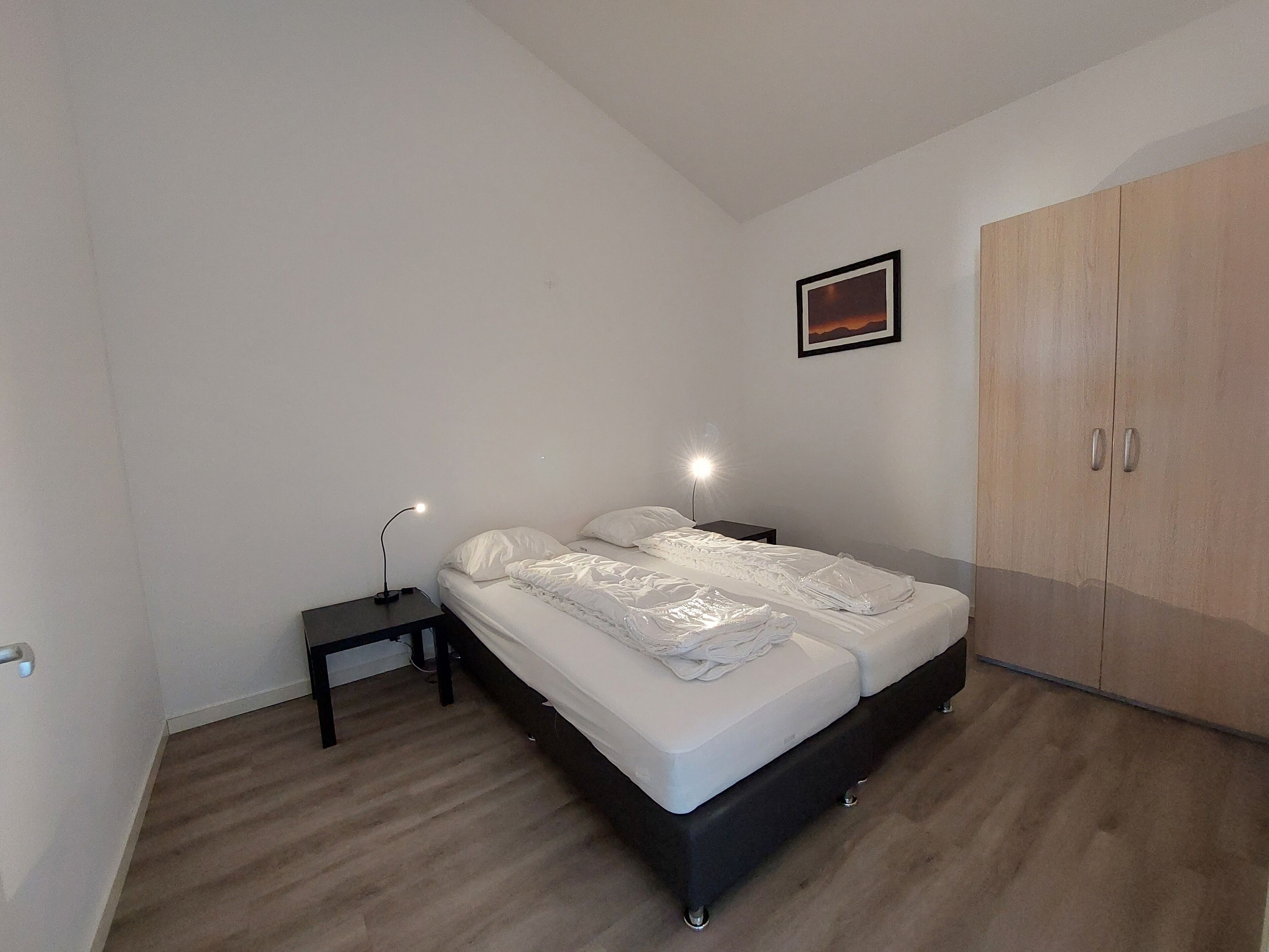 A bedroom with a bed, bedside tables, a wardrobe, and a framed picture on the wall.
