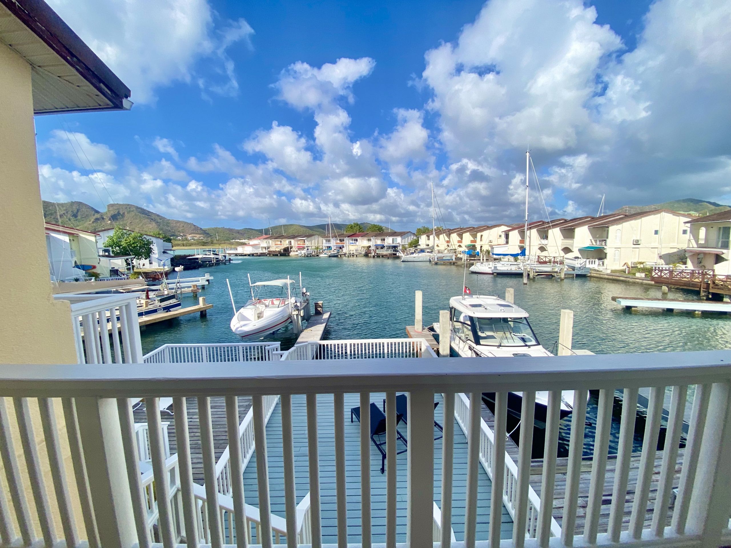 A marina with boats docked, a wooden deck, and a view of houses in the background.