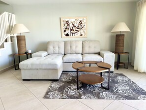 A modern living room with a sectional sofa, a round coffee table, and two floor lamps. - Enchanting Waterfront Villa (Jolly Harbour)