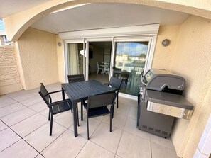 An outdoor patio with a table and chairs, a grill, and a sliding glass door leading to an indoor area. - Enchanting Waterfront Villa (Jolly Harbour)