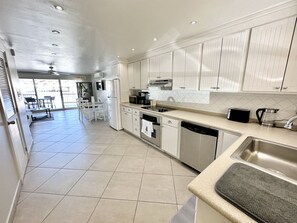 A modern kitchen with white cabinets, a stainless steel sink, and a dining area with white chairs. - Enchanting Waterfront Villa (Jolly Harbour)