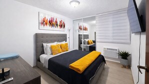 Un dormitorio moderno con una cama grande, un televisor de pantalla plana, una mesita de noche y una ventana con persianas.
