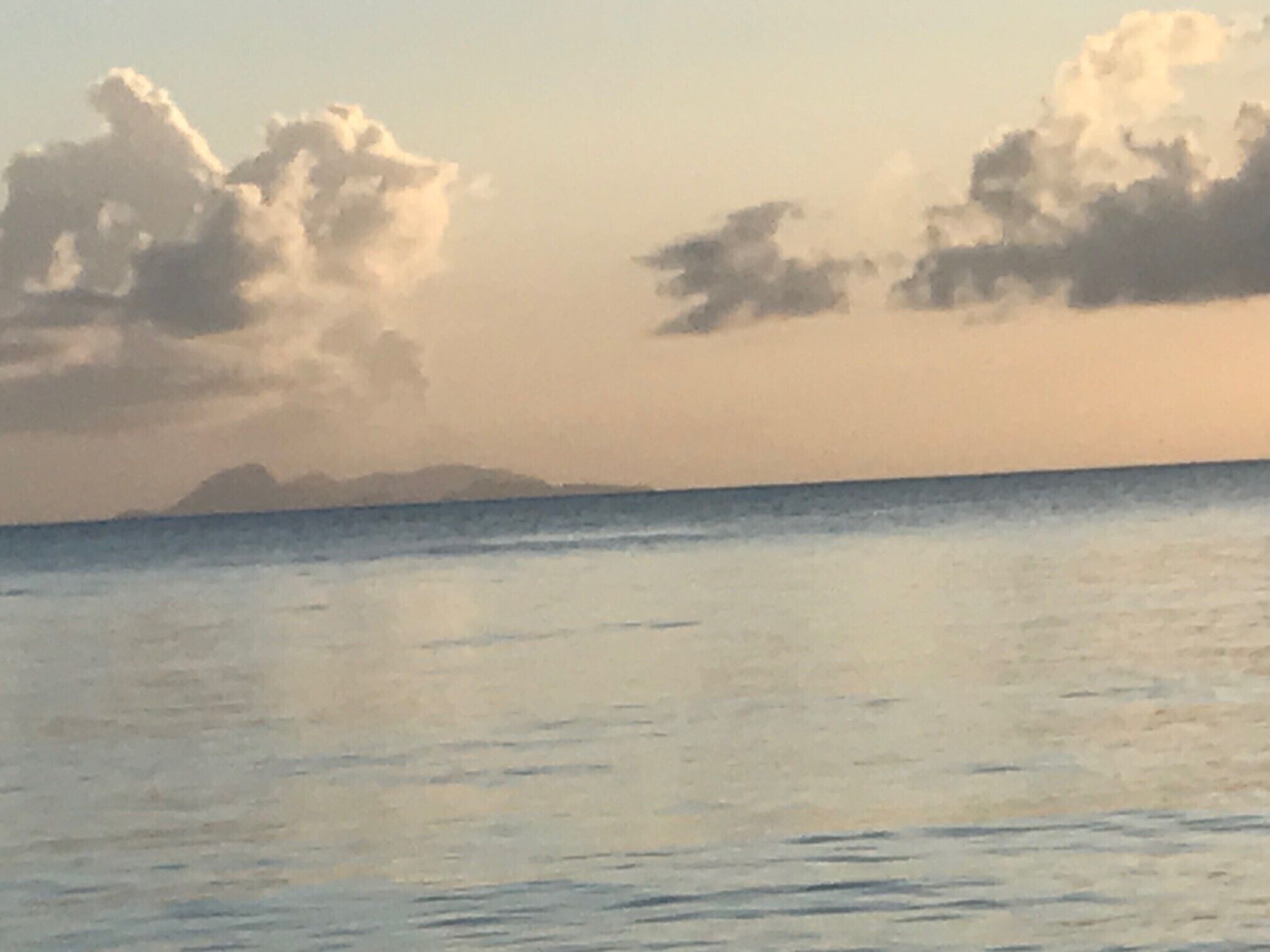 Une mer calme, avec une terre lointaine à l’horizon et quelques nuages épars.