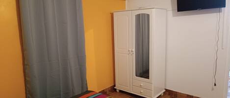 A room with a white wardrobe, a gray curtain, a colorful striped rug, and a flat-screen TV mounted on the wall.
