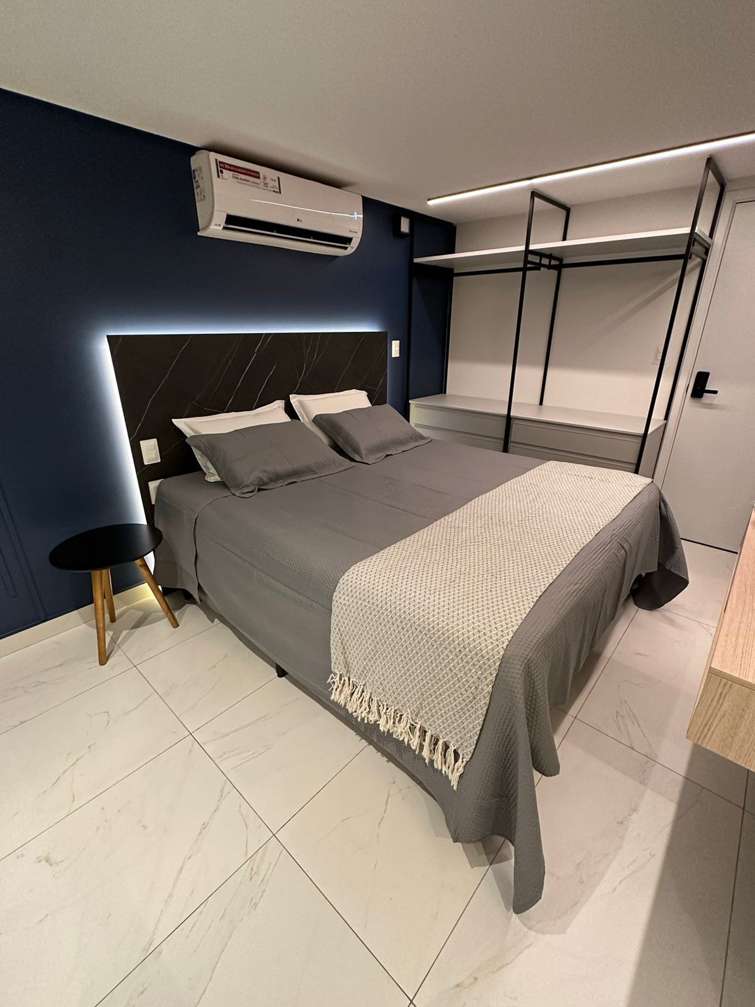 A modern bedroom with a bed, bedside tables, an air conditioning unit, and a wardrobe.