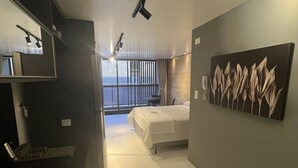 A modern hotel room with a bed, a painting on the wall, a sink, and a view of the outside. - Unity Suites (João Pessoa)