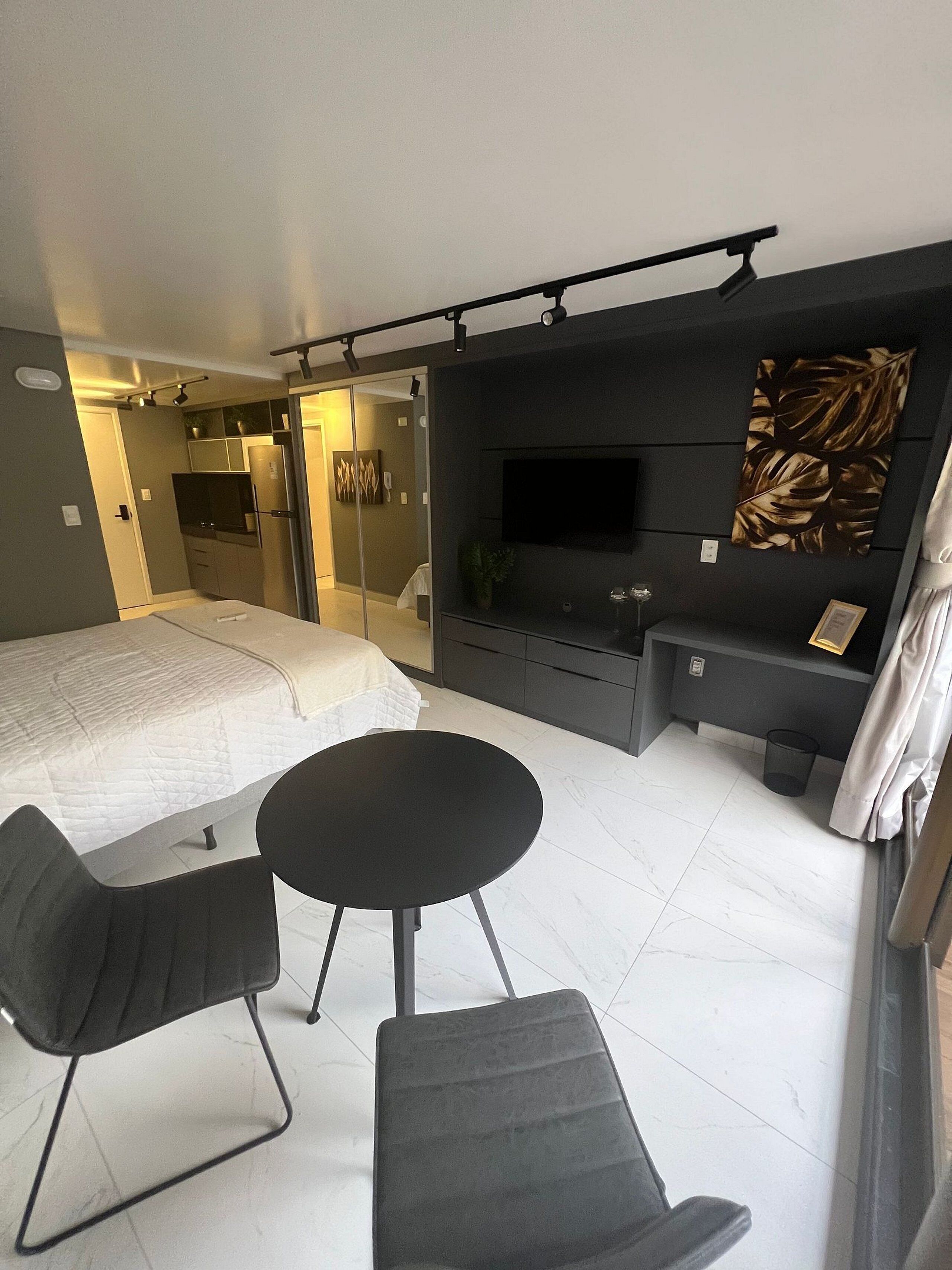 A modern hotel room with a bed, a TV, a seating area with chairs, a small table, and a plant.