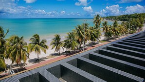A beach view with palm trees, a clear sky, and a tiled pathway. - Unity Suites (João Pessoa)