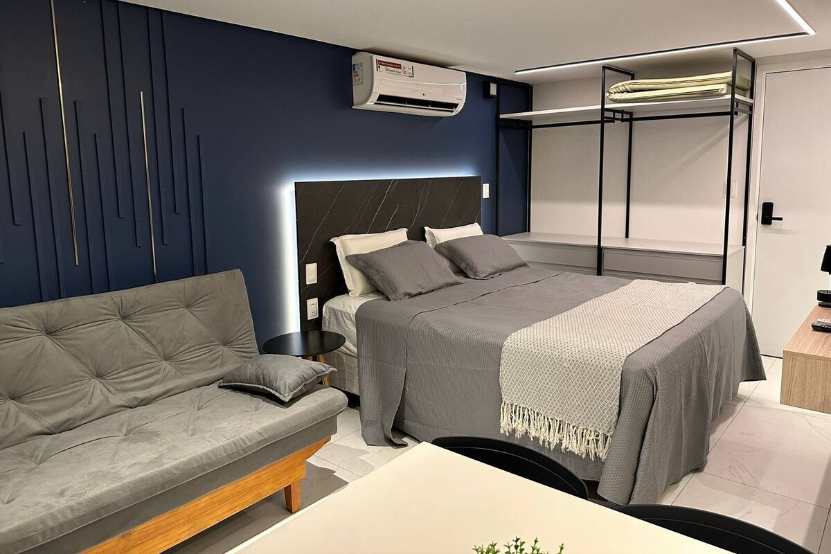 A modern bedroom with a bunk bed, a sofa, a bedside table, and an air conditioning unit.
