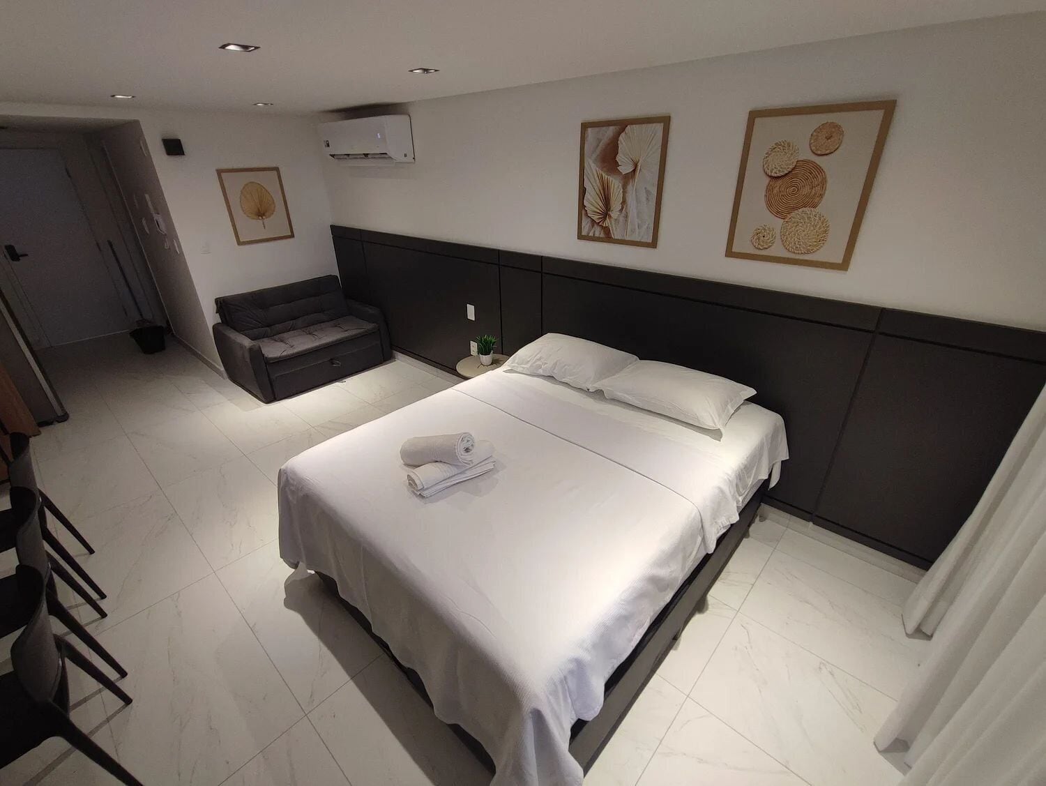 A hotel room with a bed, a sofa, a small table with a plant, and artwork on the walls.