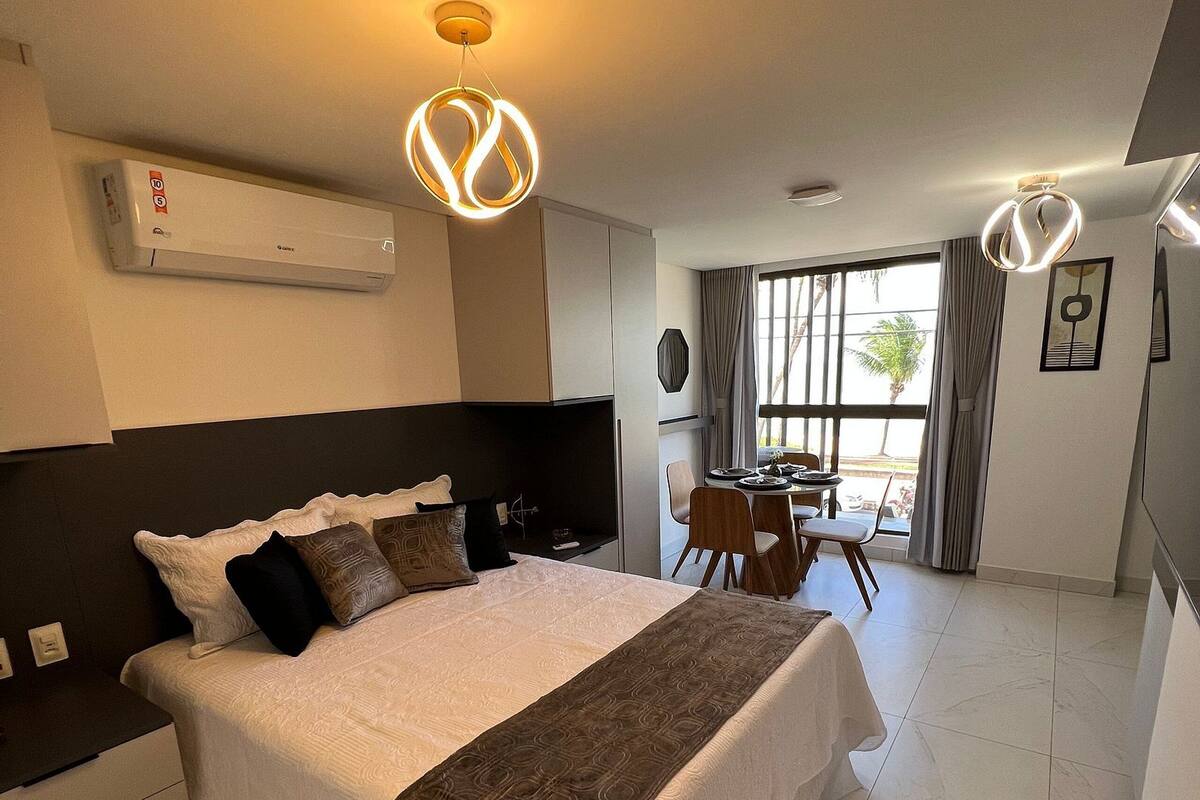 A hotel room with a large bed, a dining area, and a view of palm trees.