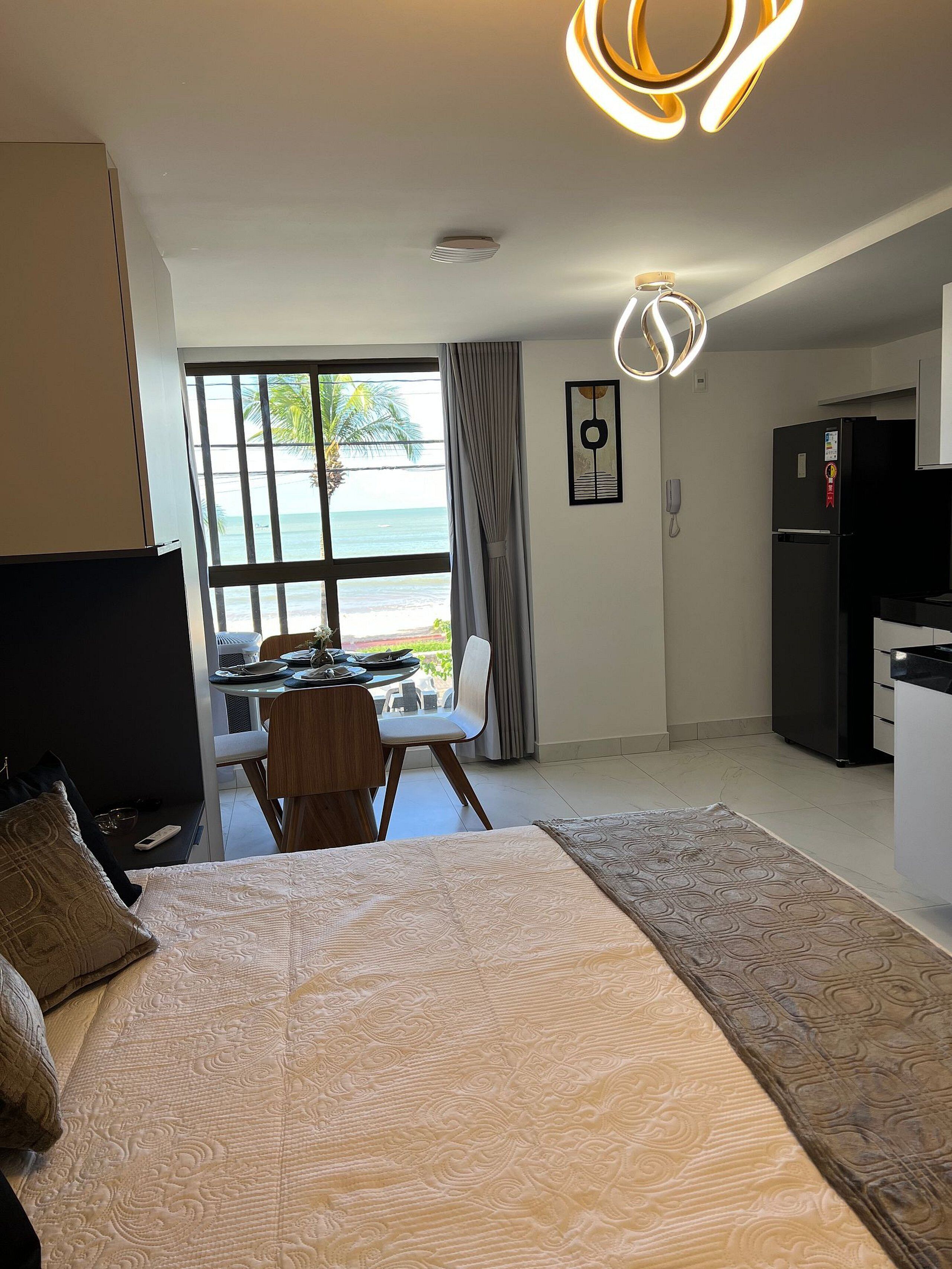 Ein Hotelzimmer mit einem Bett, einem Schreibtisch mit Stuhl, einem Kühlschrank und Blick aufs Meer.