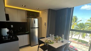 A modern kitchen with a dining area, a refrigerator, and a view of palm trees. - Unity Suites (João Pessoa)