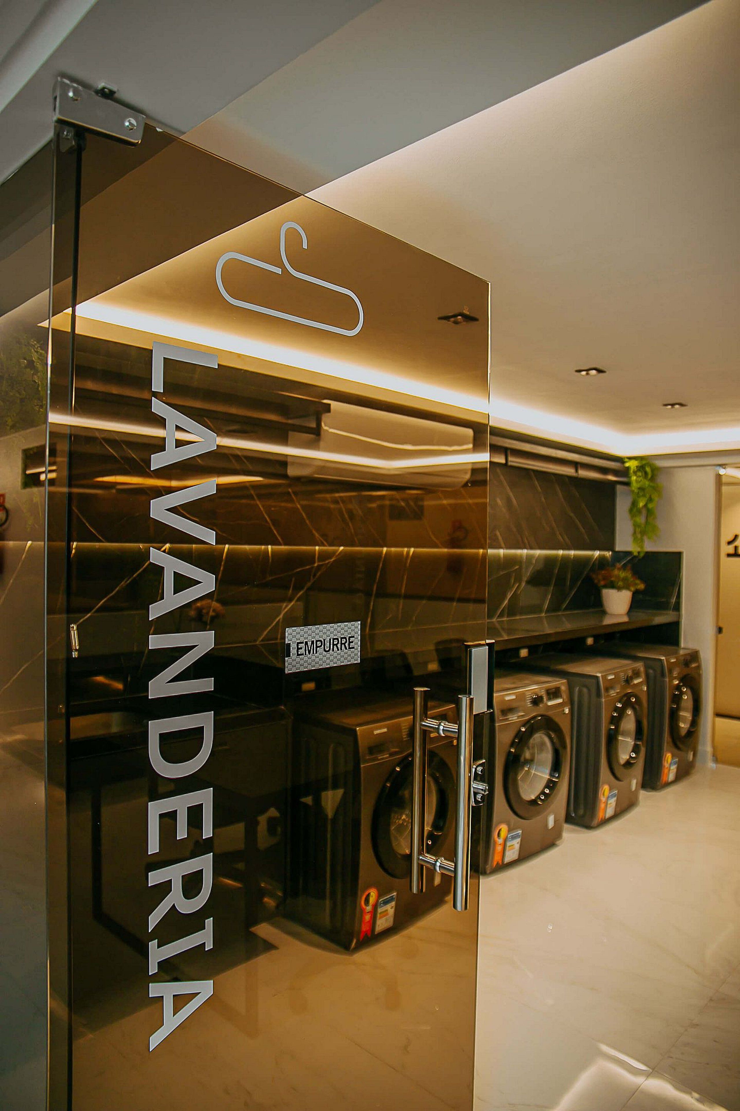 Una lavandería moderna con puertas de vidrio, un letrero visible que dice 'LAVANDERIA' y varias lavadoras.