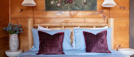 A wooden-paneled room with a bed, two lamps, a vase with flowers, and a painting on the wall.