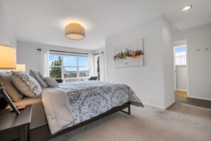 Quarto com cama, mesa de cabeceira, abajur e janela com cortinas.
