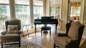 A room with a piano, two armchairs, a small table, and large windows.