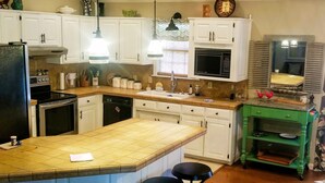 A kitchen with white cabinets, a green island with stools, a microwave, and a stove.