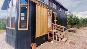 Una casa moderna de dos pisos, con ventanas amplias, una puerta de madera y un pequeño espacio exterior con asientos.