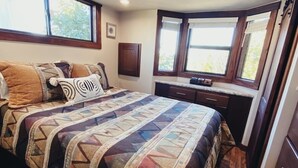 Un dormitorio con una cama grande, suelo de madera, una ventana con persianas y una zona de escritorio integrada.